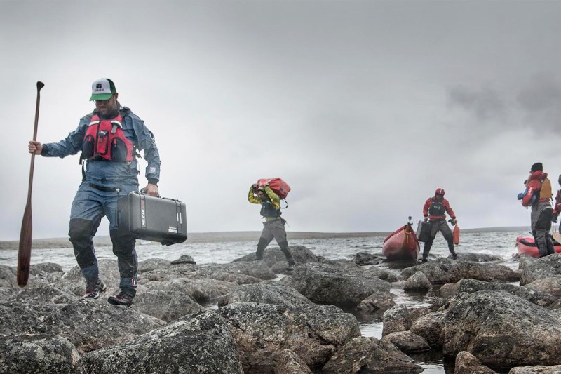 Paddlers standing on boulders near the ocean with their outdoor gear.