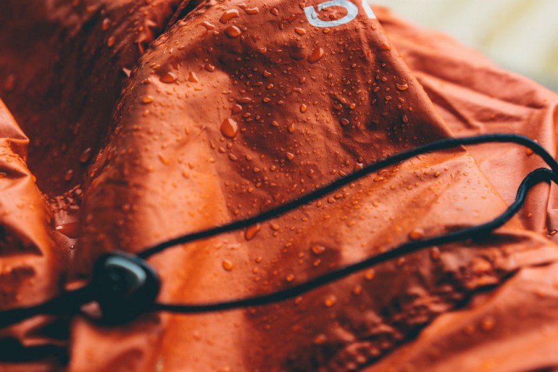 An orange waterproof jacket with rain droplets on it.