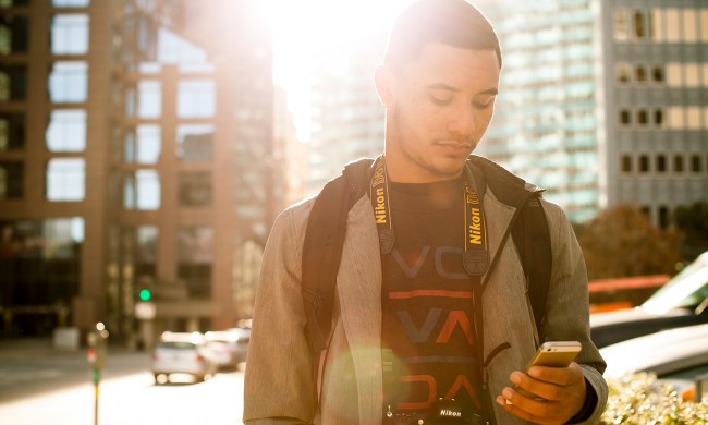 A man looks at his phone while exploring the city on a sunny day.