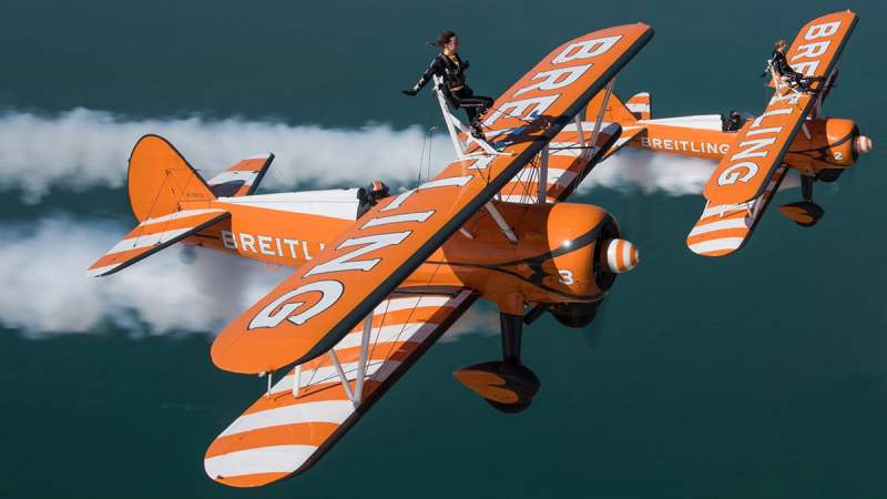 Pair of vintage biplanes with daredevils wing walking on their wings.