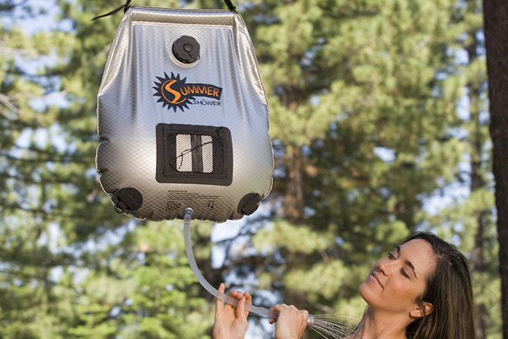 Woman using a solar shower under trees while camping.