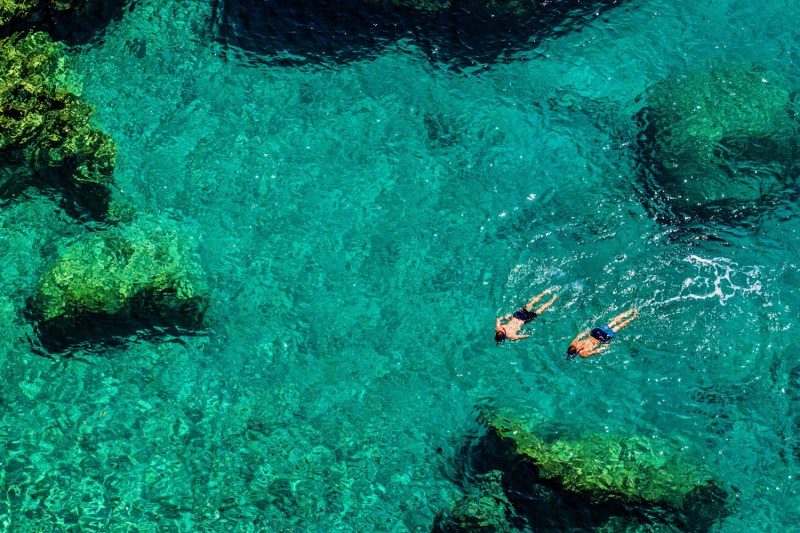 Aerial view of two men snorkeling in clear, shallow tropical water.
