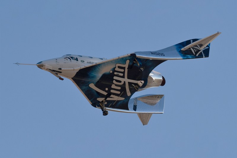 Virgin Galactic aircraft in flight against a clear blue sky.