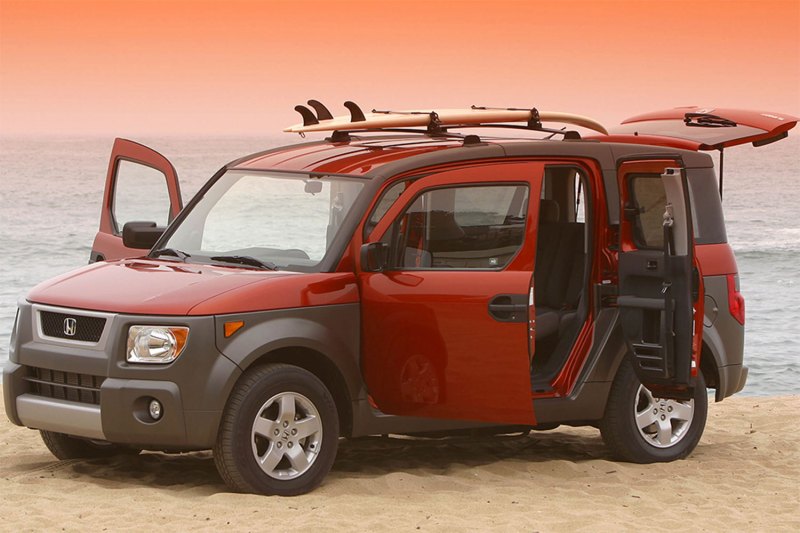 Red and Black Honda Element parked in a sandy road.