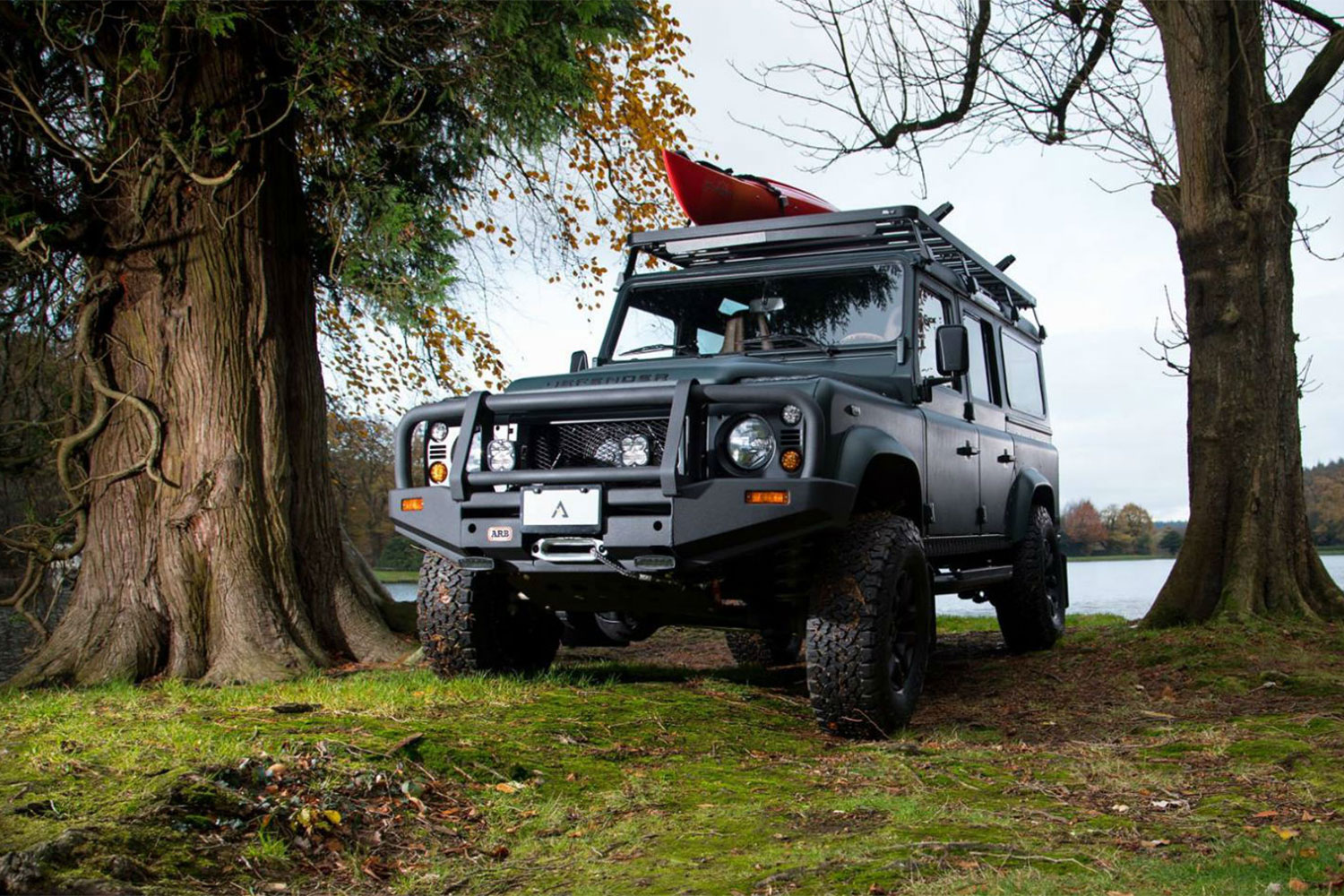 Black Land Rover Defender parked in between trees.