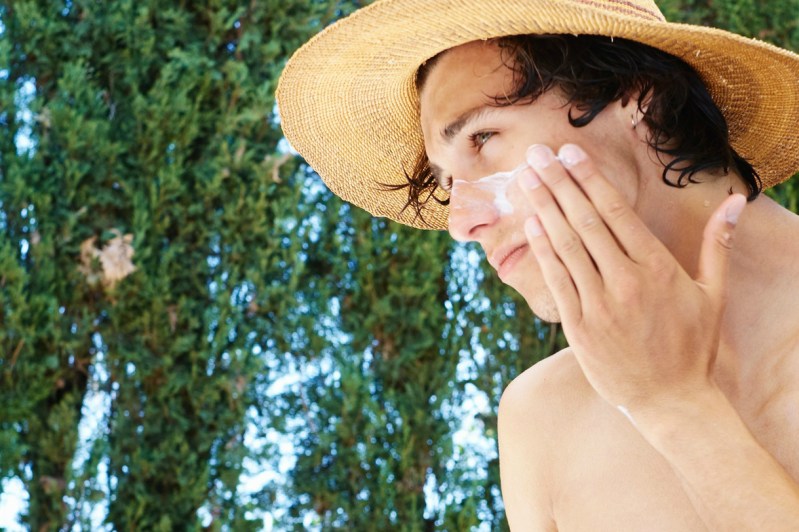Man applying sunscreen to face with straw hat