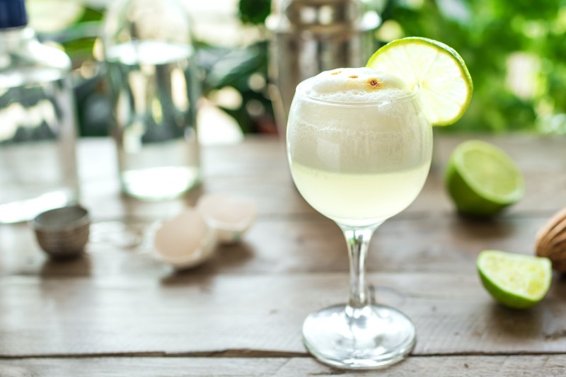 A cold glass of Pisco sour cocktail with lime on a wooden table