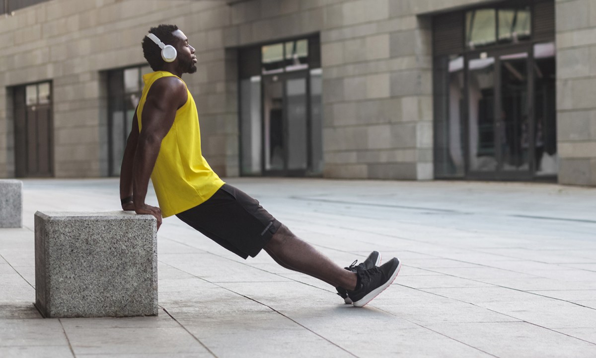 Man leaning against a concrete block doing dips.