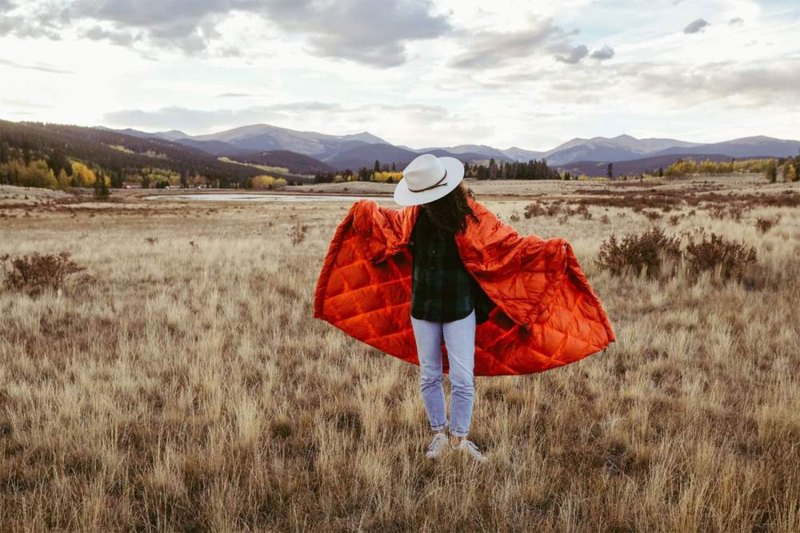 person standing in a field with blanket over their shoulders.