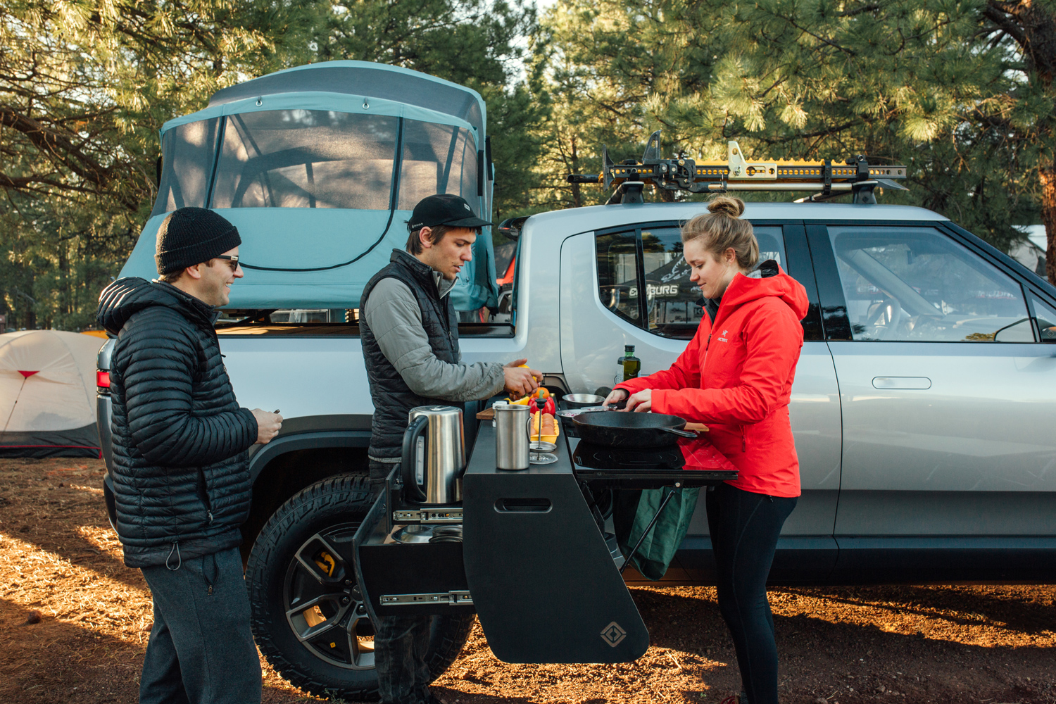 Three people cooking using a camp kitchen next to Rivian R1T