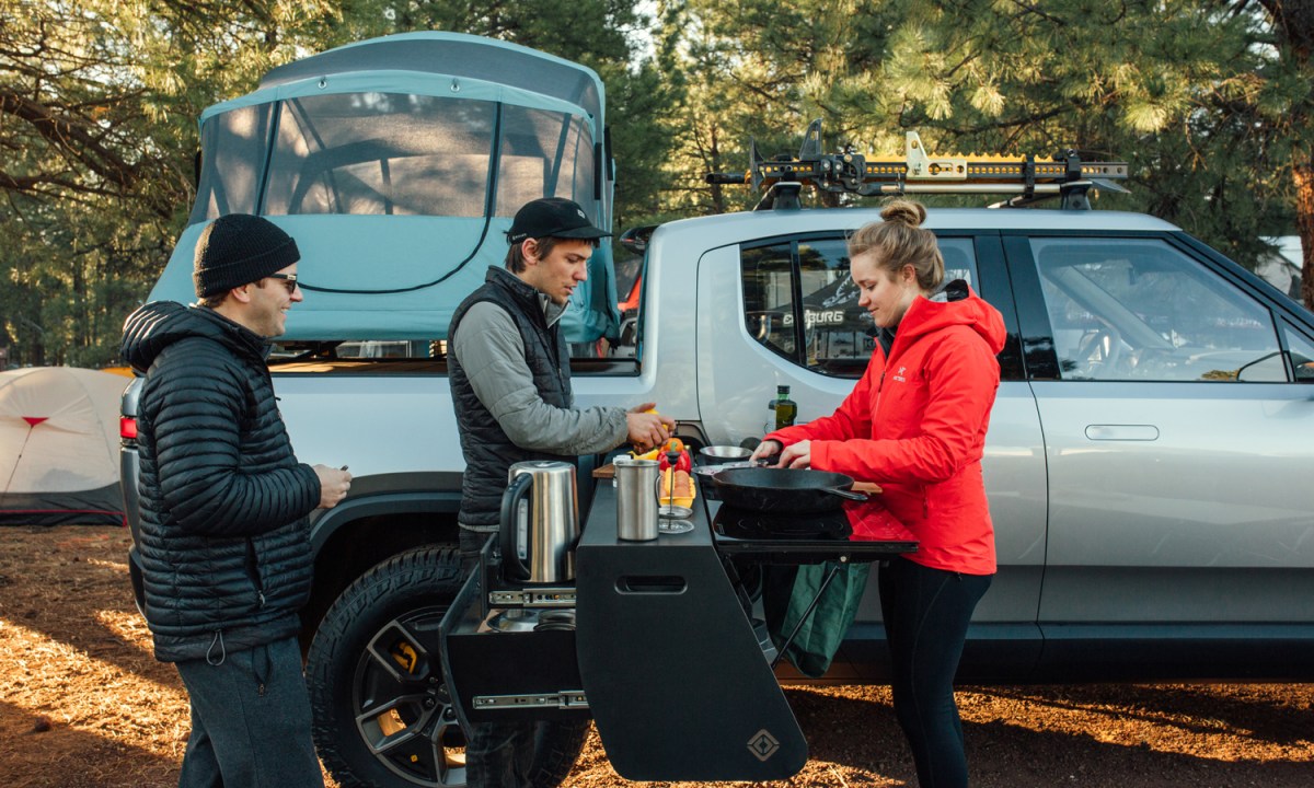 Three people cooking using a camp kitchen next to Rivian R1T