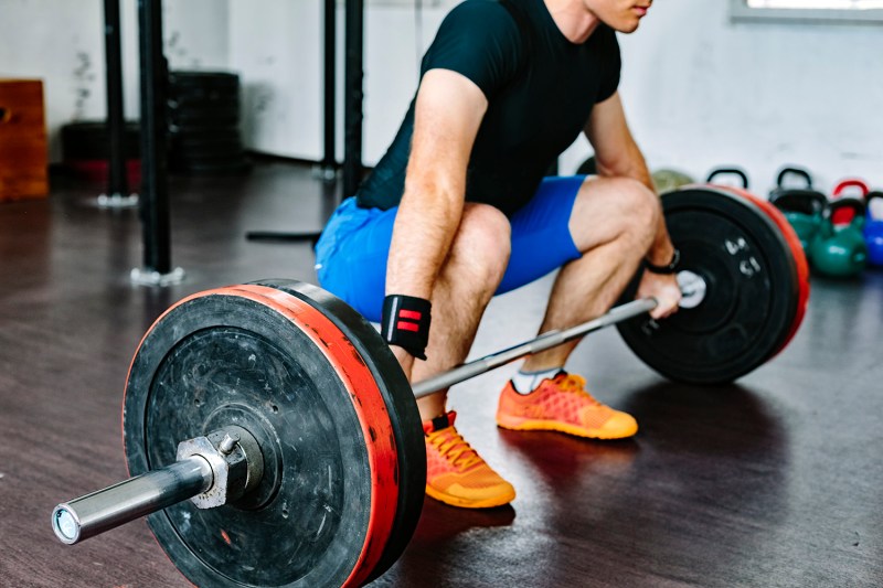 A man wearing a black shirt as he does a deadlift in the gym.