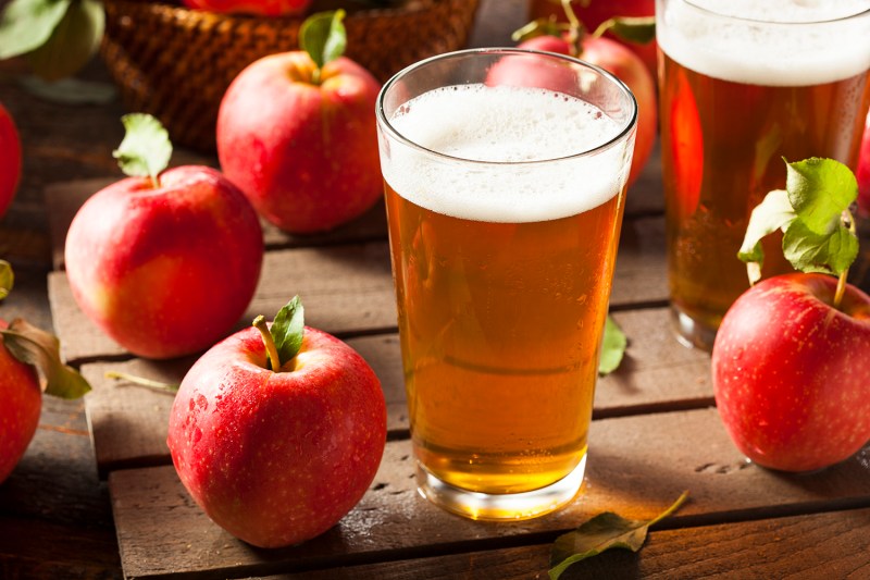 A glass of apple cider surrounded with apples.