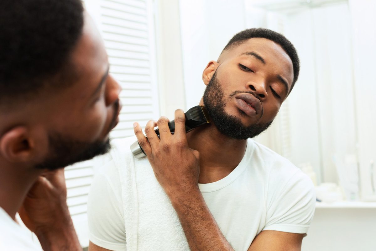A man trimming his beard in the mirror.