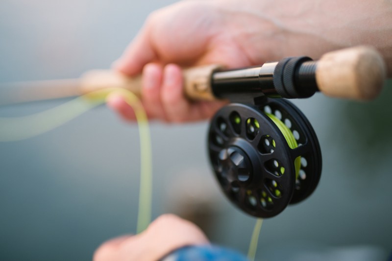Closeup of two hands working a fly fishing rod and reel.