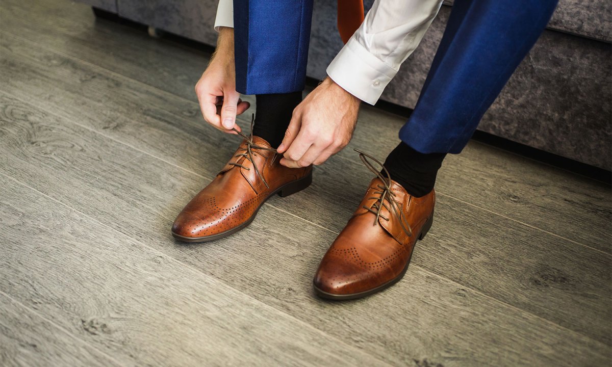 A man tying the shoelaces of his leather dress shoes.