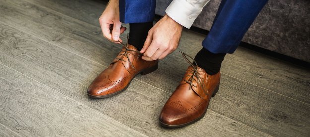 A man tying the shoelaces of his leather dress shoes.