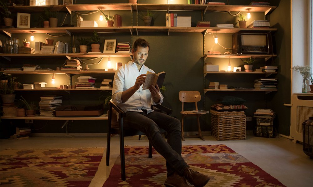 A man sitting on a chair and reading a book in home library