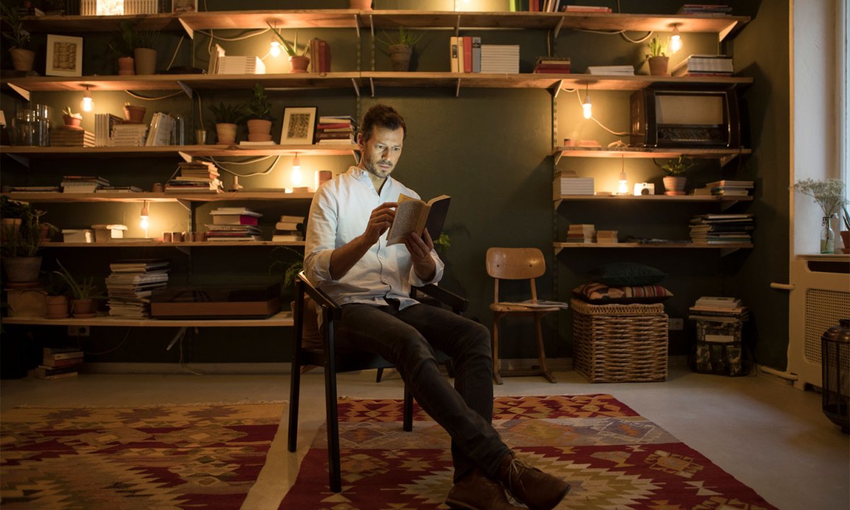 A man sitting on a chair and reading a book in home library