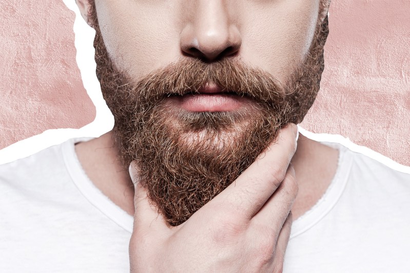 A man in white t-shirt touching his beard.