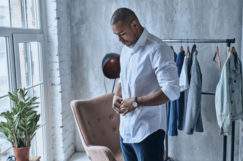 A man getting dressed, buttoning up his shirt.