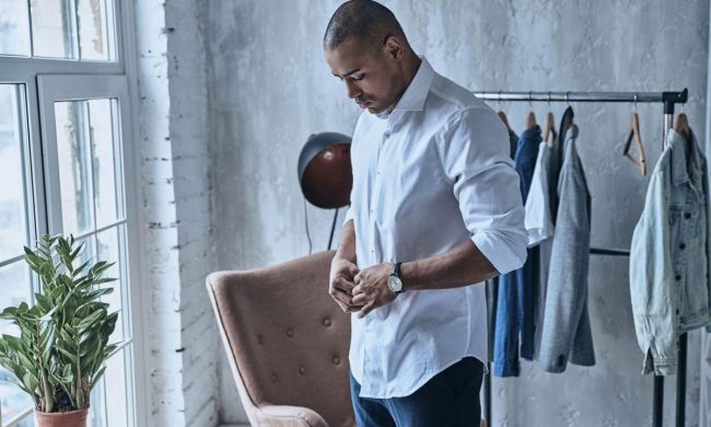 A man getting dressed, buttoning up his shirt.
