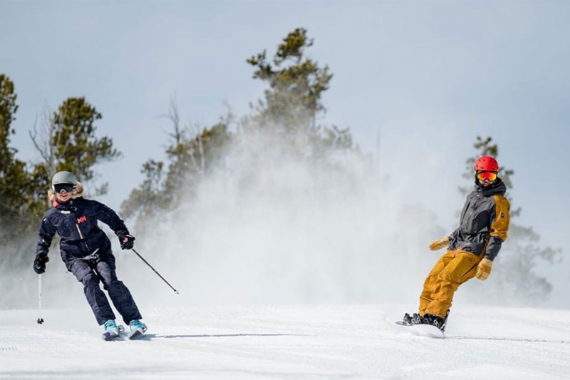 A skier and a snowboarder coming down a snowy mountain together toward the camera.