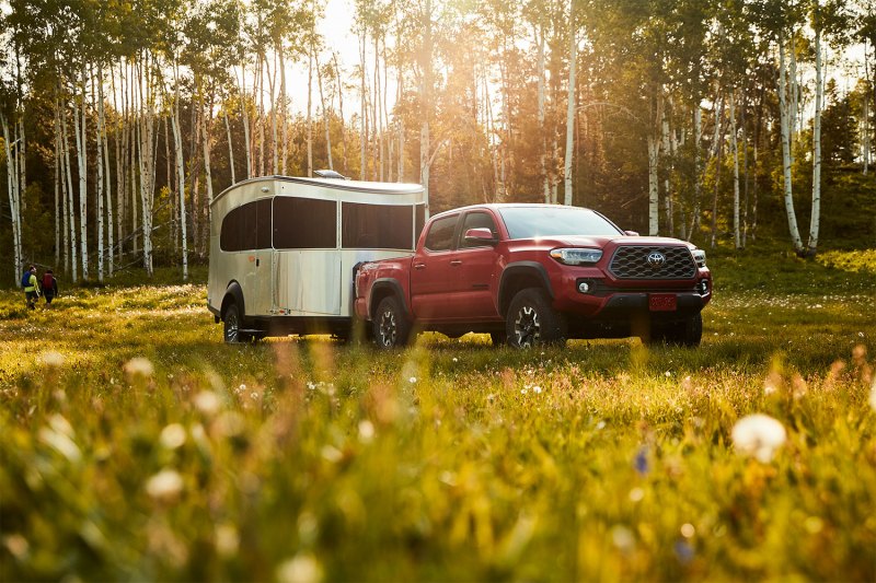 Red Toyota Tacoma towing an Airstream Basecamp throw a grassy field.