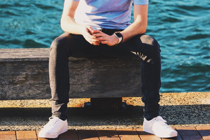 A man sitting on a concrete seat, wearing white sneakers.