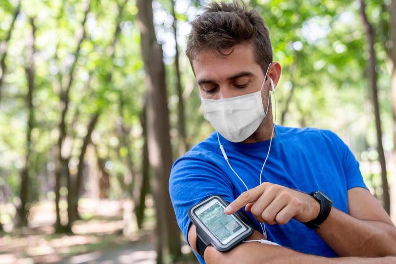 Man running outdoors wearing a facemask and using an arm band for his cell phone