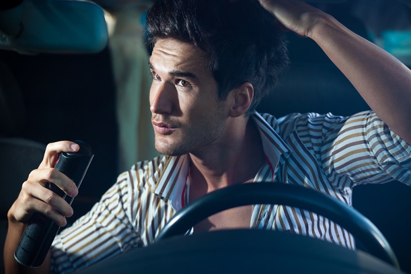 A man using dry shampoo inside a car. 