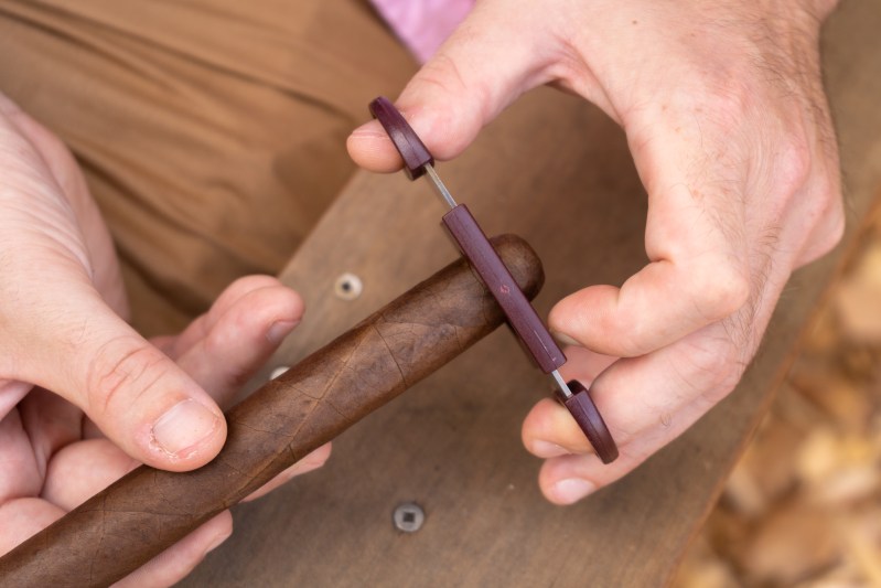 Close-up of hands cutting a cigar with a cigar cutter.