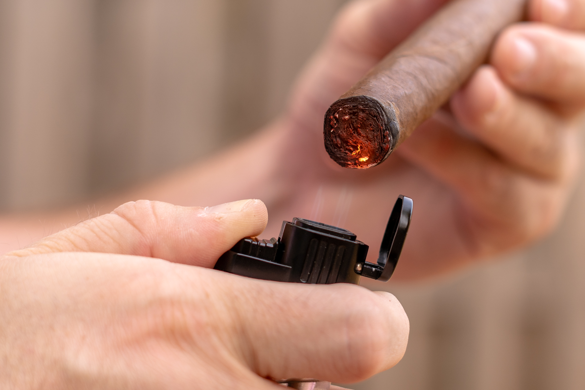 Close-up of someone lighting a cigar with a lighter.