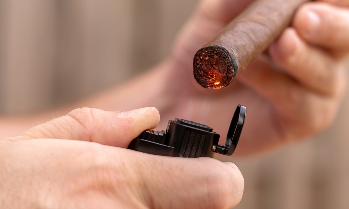 Close-up of someone lighting a cigar with a lighter.