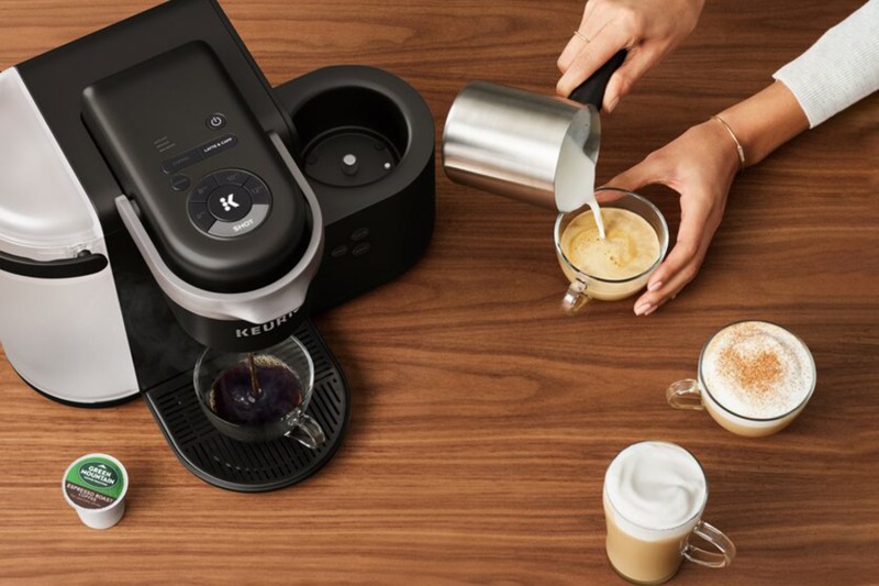 Keurig K Cafe brewing coffee with a woman pouring milk into a coffee cup.