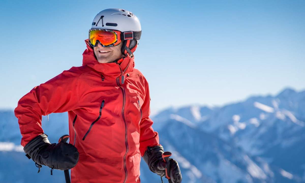 Smiling nan in a red ski jacket and helmet standing on a ski slope.