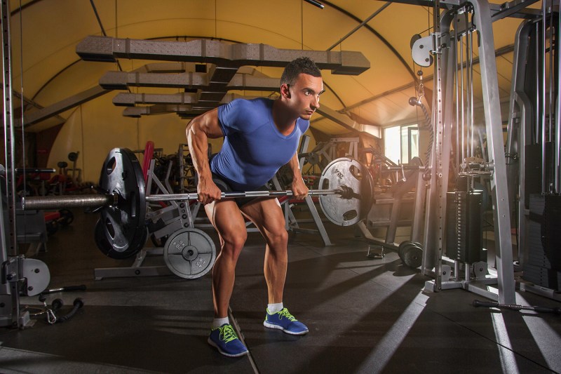 Man wearing a lilac dry-fit shirt and workout shorts as he is trying to do a back row.
