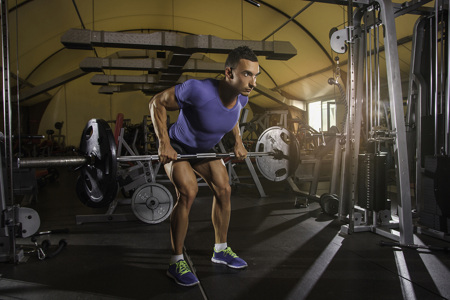 Man wearing a lilac dry-fit shirt and workout shorts as he is trying to do a back row.