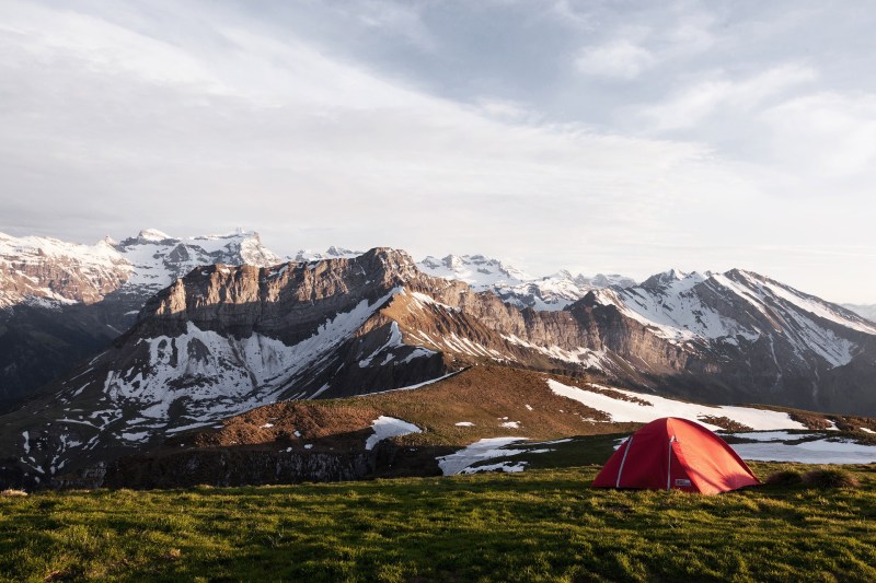 A camping tent on a grassy field near snowy mountains.