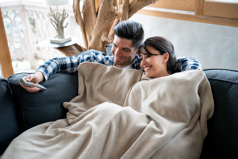 man and woman lying on a couch with a blanket.