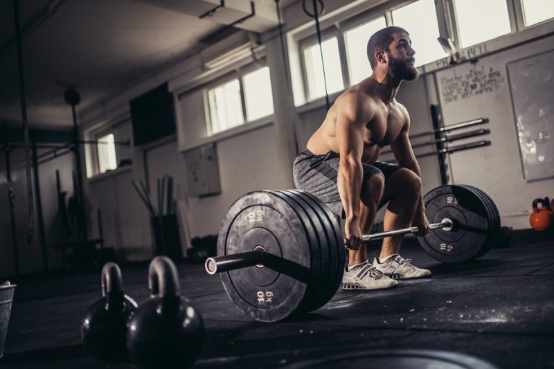 Man with a buzzcut at an empty gym preparing to do a sumo-style dead lift.