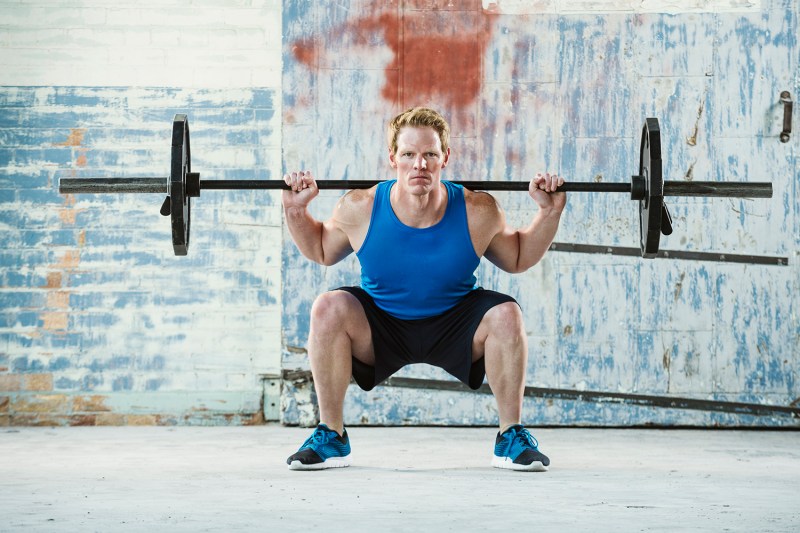 Muscular man weightlifting and doing a back-loaded squat with his knees slightly bent.