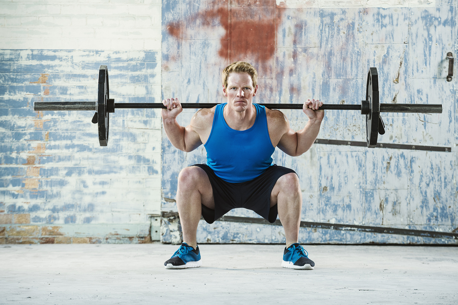Muscular man weightlifting and doing a back-loaded squat with his knees slightly bent.