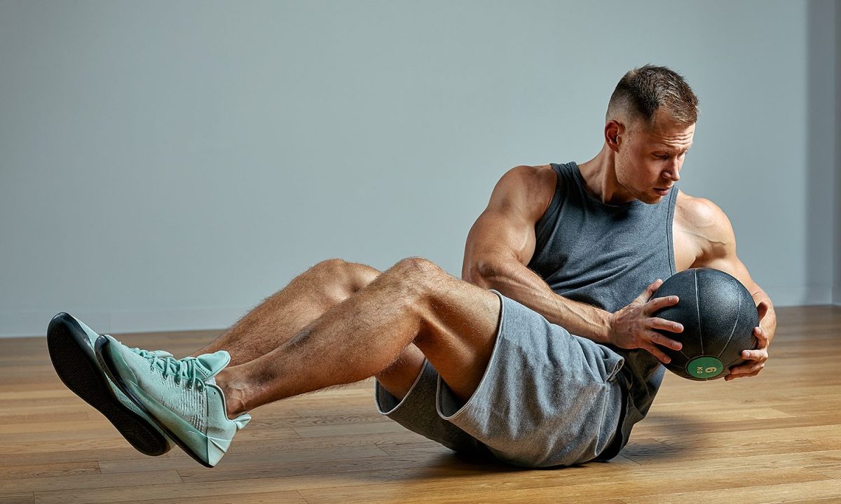 A man doing a Russian twist while holding a medicine ball