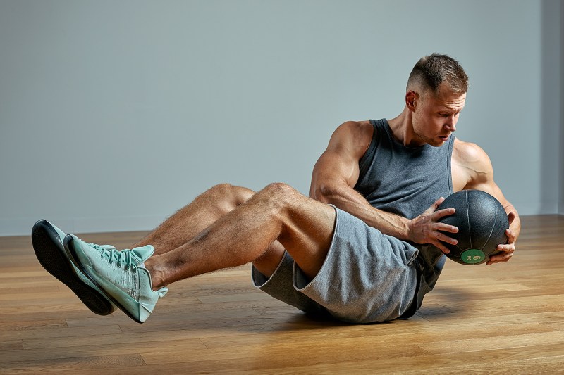 A man doing a Russian Twist while holding a medicine ball.