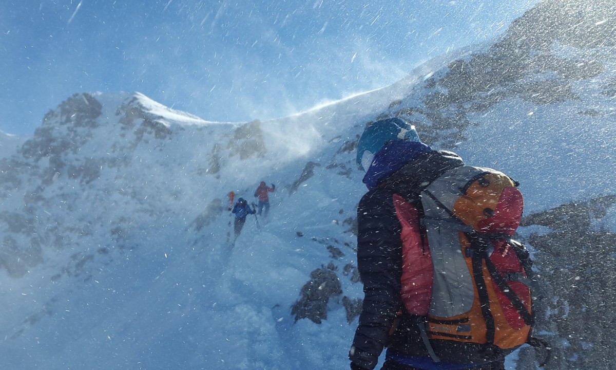 Three hikers with ski backpacks scaling a snow-capped mountain.