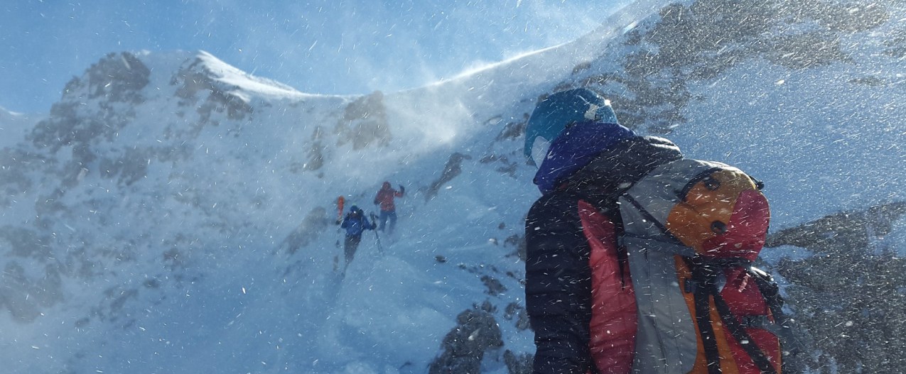 Three hikers with ski backpacks scaling a snow-capped mountain.