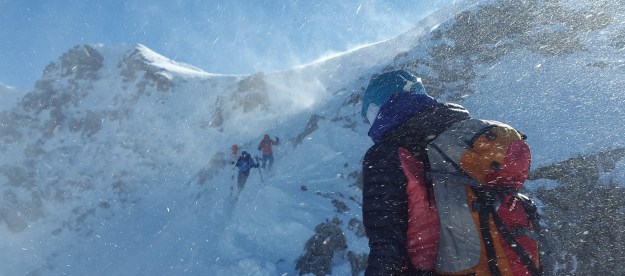 Three hikers with ski backpacks scaling a snow-capped mountain.