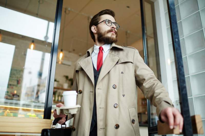 Man dressed in coat holding a cup of coffee.