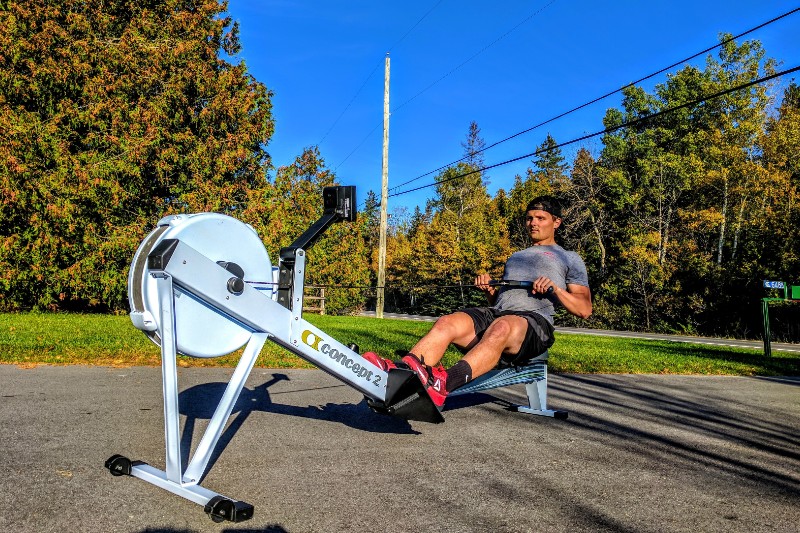 A male athlete using a rowing machine outside.